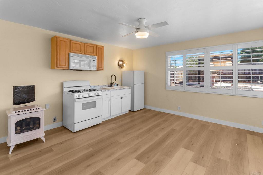 Vacant kitchenette with white appliances, light wood floors, and a wide shuttered window.