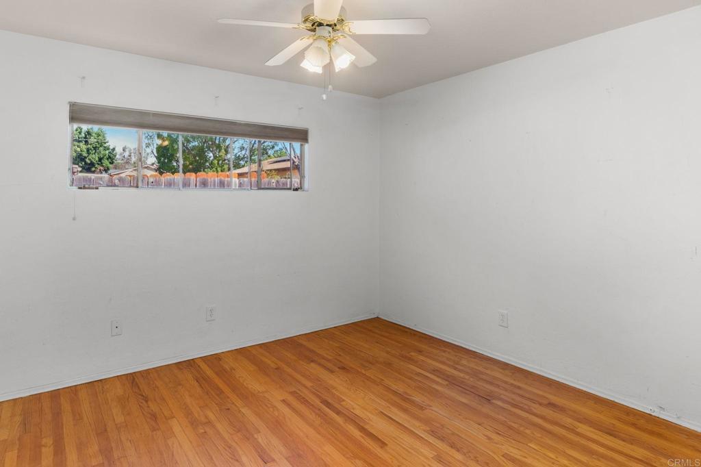 Empty room with hardwood floors, a wide window, and a ceiling fan with lights.