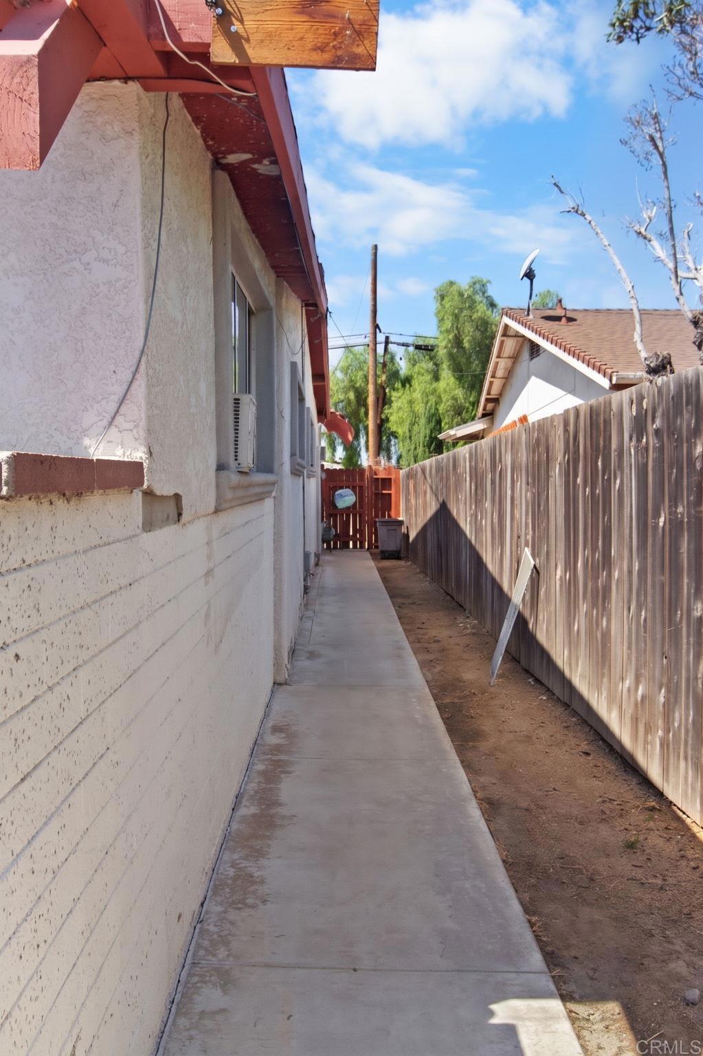 Side yard with a concrete walkway running between the stucco house and a tall wooden fence.