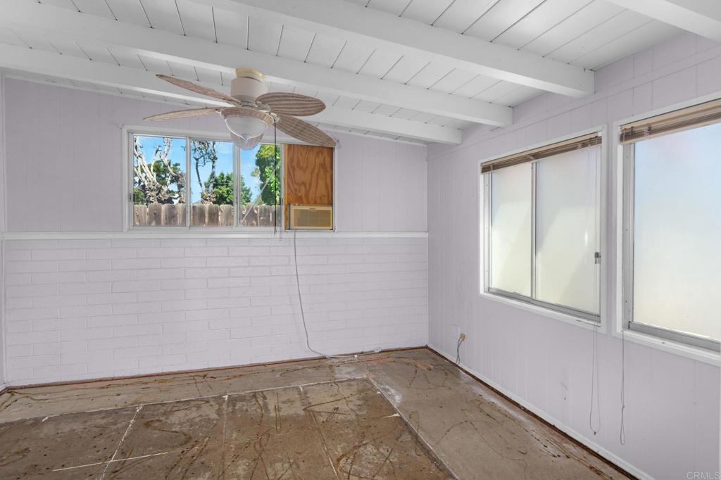 Empty room with a ceiling fan, multiple windows, and a worn bare floor.