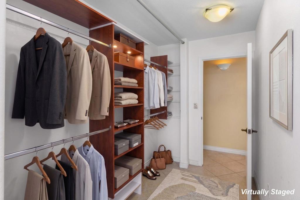 Walk-in closet with built-in wooden shelving, hanging clothes, folded towels, and a tiled entry.