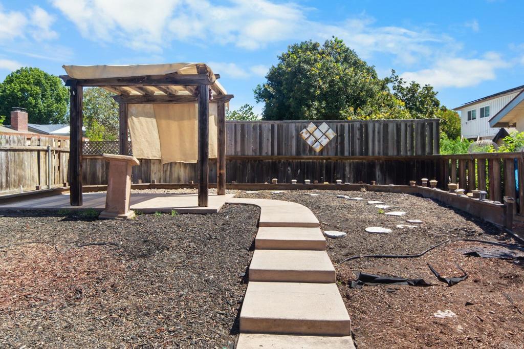 Backyard with a wooden pergola, curved concrete path, mulch, and tall privacy fencing.