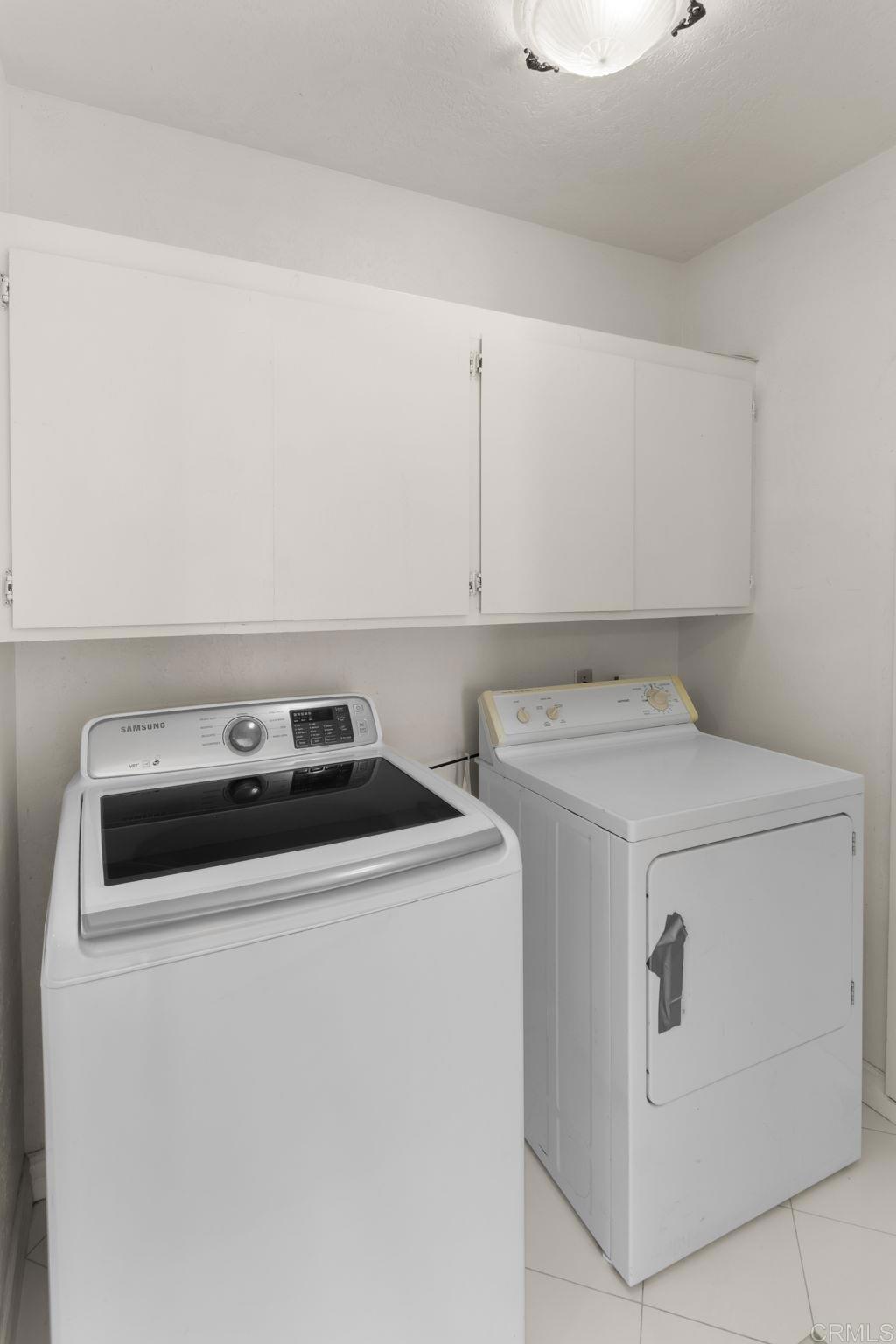 Laundry room with a Samsung washer, white dryer, and overhead storage cabinets.