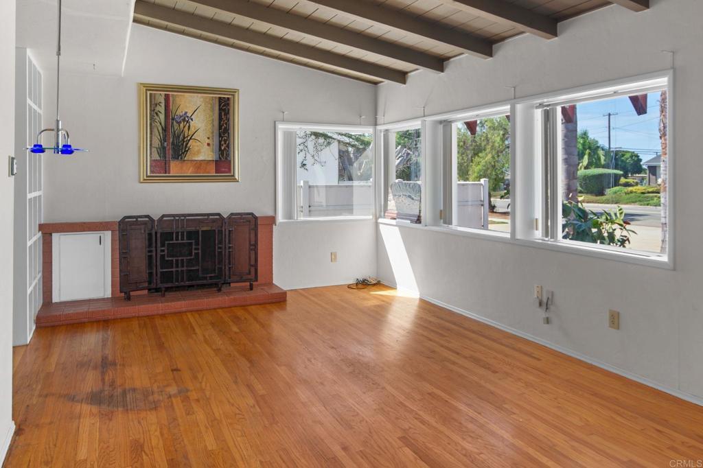 Living room with hardwood floors, exposed beams, a brick fireplace, and large street-facing windows.