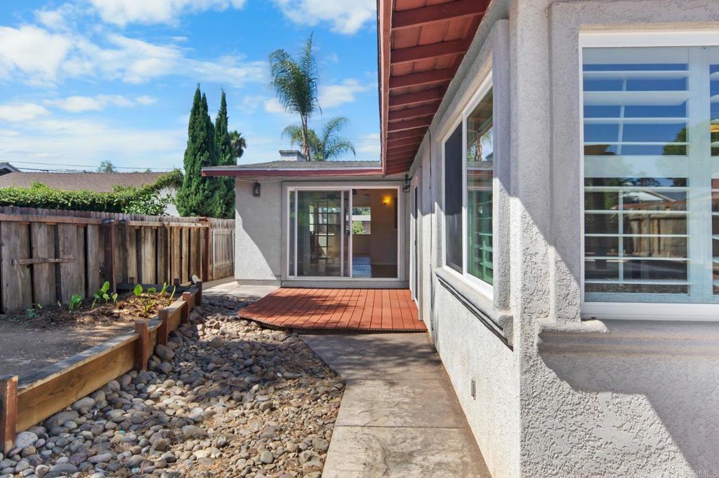 Side yard with a redwood patio deck, sliding glass door, rock landscaping, and fenced garden bed.