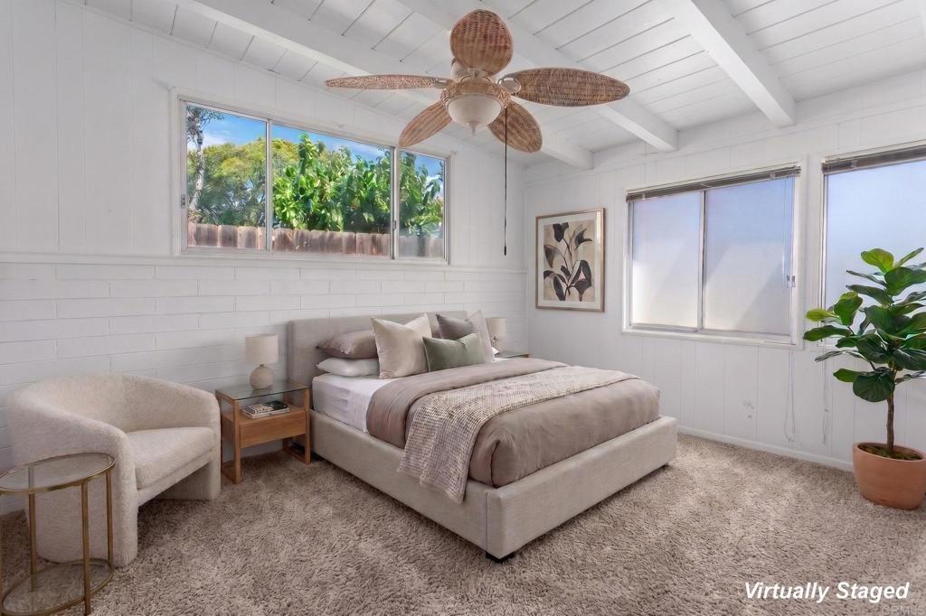 Virtually staged bedroom with a white bed, upholstered chair, and large windows overlooking greenery.