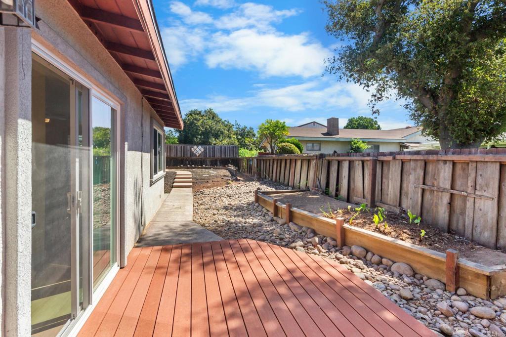 Backyard deck beside a gravel path and raised garden beds, enclosed by a wooden fence.