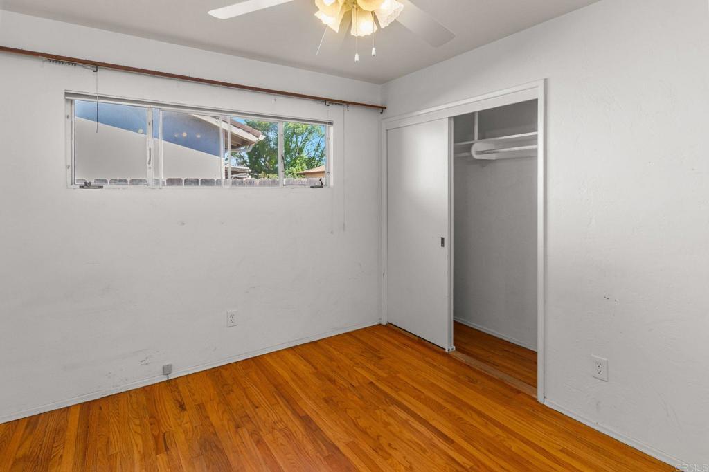 Empty bedroom with hardwood floors, a wide window, and a sliding-door closet.
