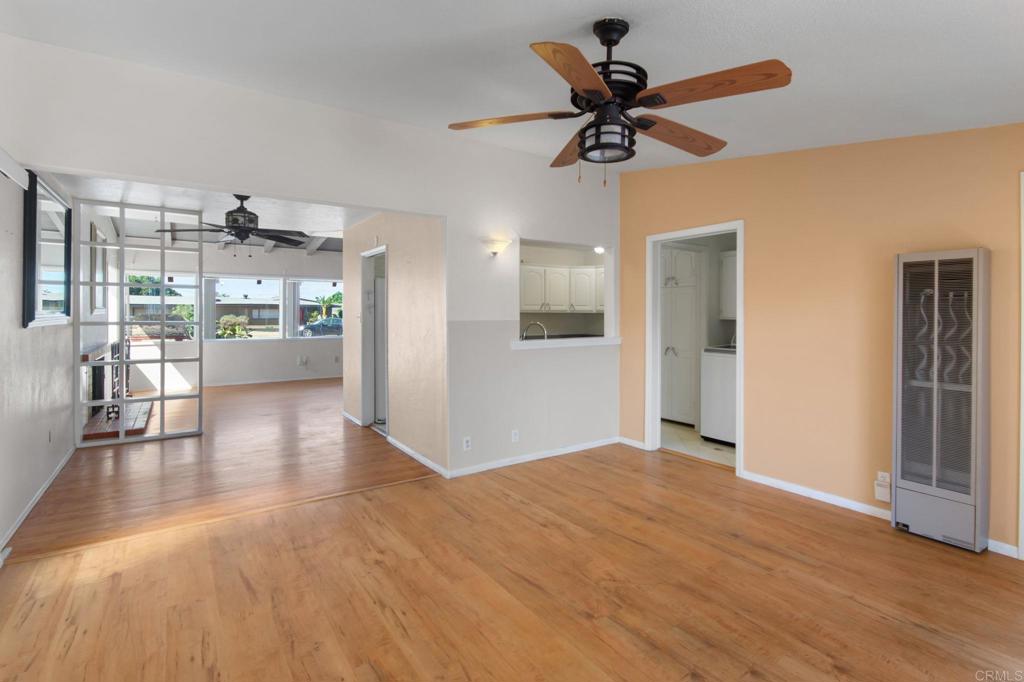 Living area with wood flooring, a ceiling fan, peach accent wall, and pass-through to the kitchen.