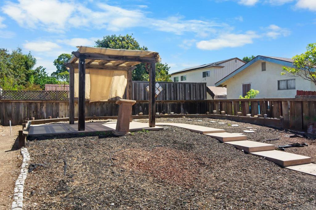 Fenced backyard with a wooden pergola and stepping-stone path across a gravel yard.