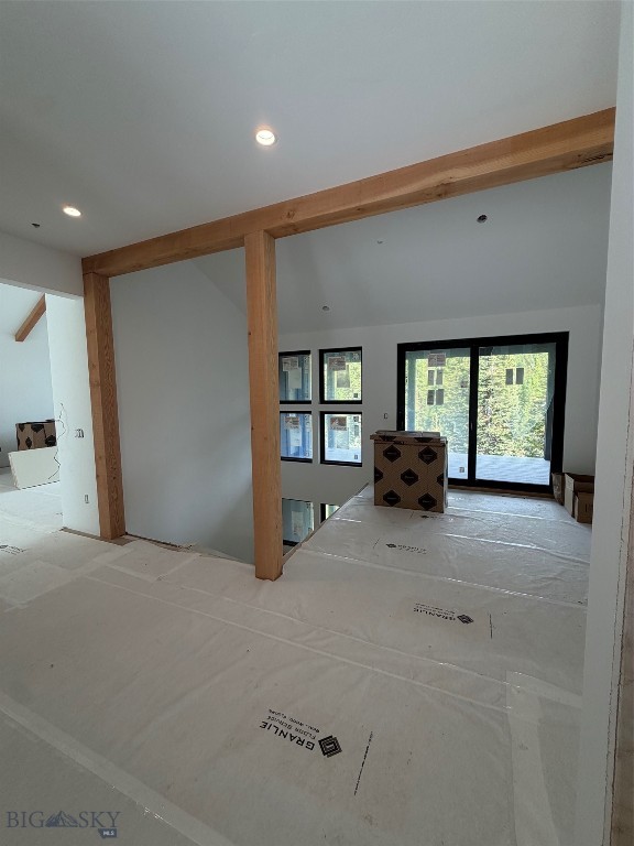 Unfinished interior with exposed timber beams, covered floors, and black-framed windows overlooking trees.