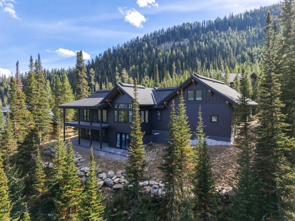 Dark gray mountain home among evergreens, with a forested mountain behind it.