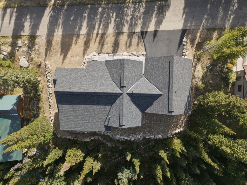 Aerial view of a gray-roofed house surrounded by trees, with a road along the property.