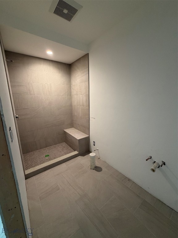Unfinished bathroom with a tiled walk-in shower, built-in bench, and exposed sink plumbing.