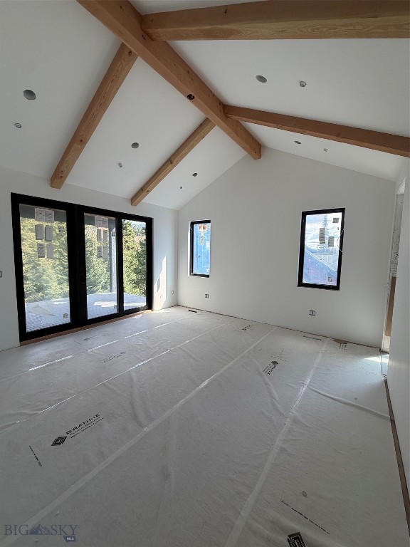 Unfinished room with exposed timber ceiling beams, black-framed glass doors, and floor protection.