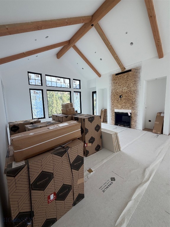 Living room under construction with exposed timber beams, tall windows, and a stone fireplace.