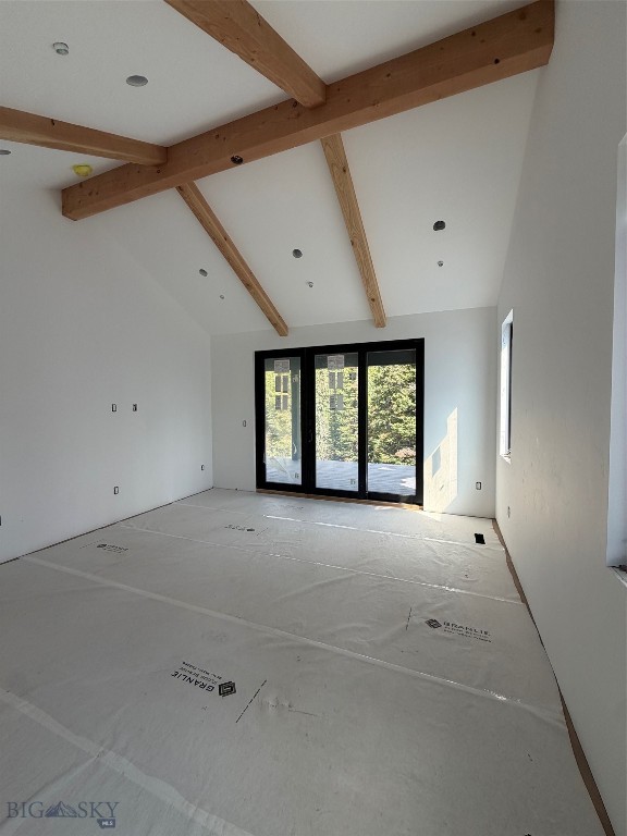 Unfinished room with exposed timber beams, floor protection, and black-framed sliding glass doors.
