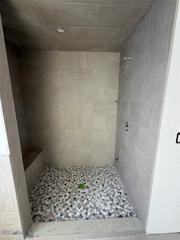 Walk-in shower with a pebble mosaic floor, gray tile walls, built-in bench, and recessed niche.