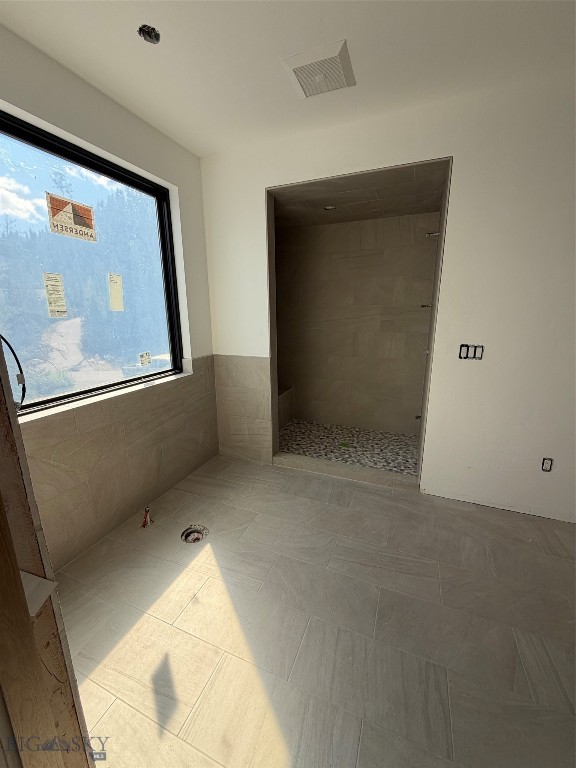 Unfinished bathroom with a tiled walk-in shower, large window, and sunlight on the floor.