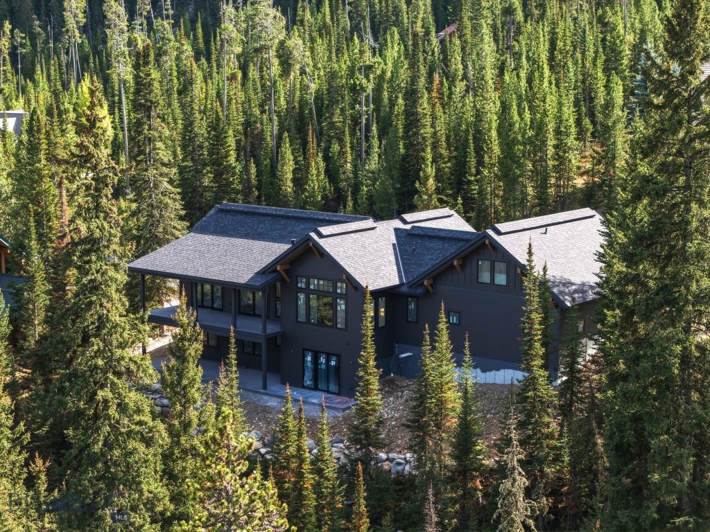 Dark-sided mountain home with multiple gabled roofs nestled among dense evergreen trees.