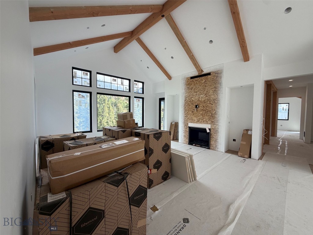 Unfinished living room with vaulted timber ceiling, forest-view windows, fireplace, and stacked building materials.