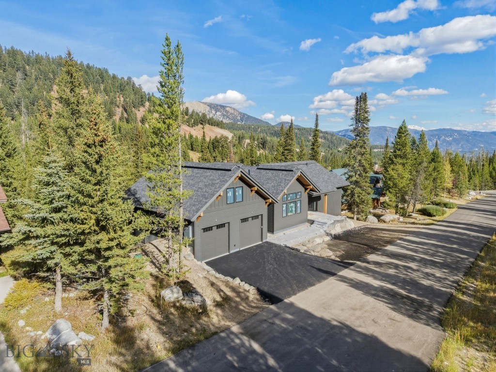 Elevated view of a gray mountain home with gabled roof, driveway, and forested mountains.