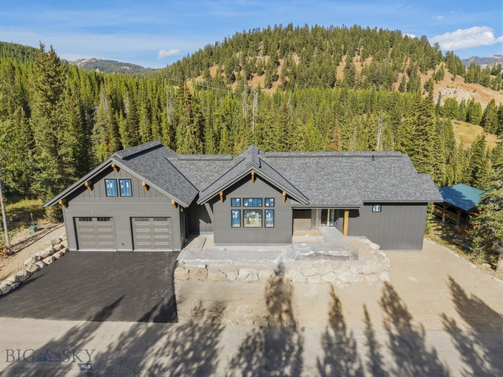 Gray mountain home with a two-car garage, backed by evergreen forest and wooded hills.
