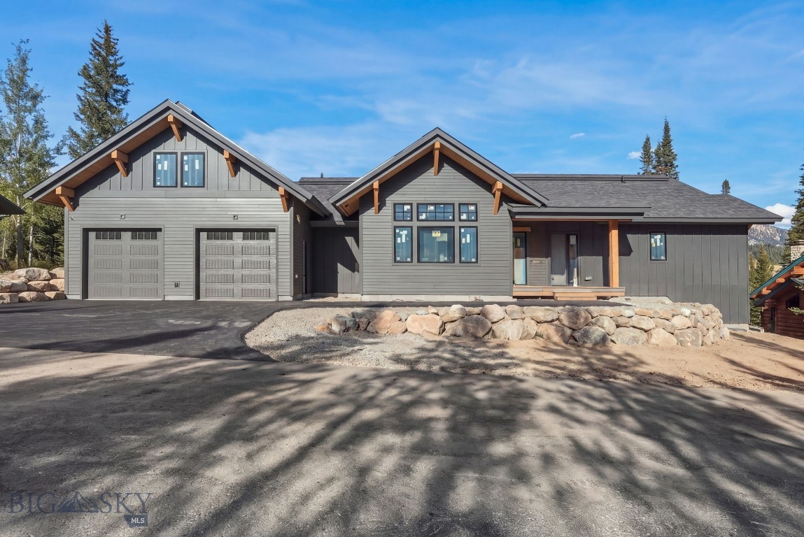 Modern gray home with twin garage doors, timber accents, and a stone retaining wall.