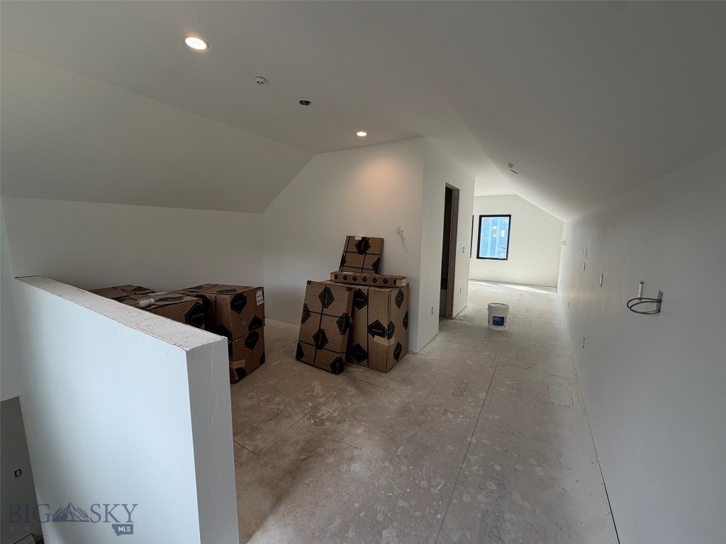 Unfinished upper-level interior with sloped ceilings, bare subfloor, and boxed building materials.