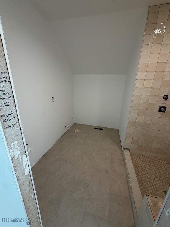 Unfinished shower area with gray floor tile and beige tiled walls.