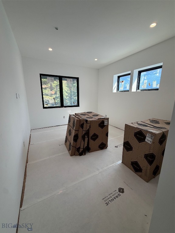 Unfinished interior room with protective floor covering and boxed building materials beneath three windows.