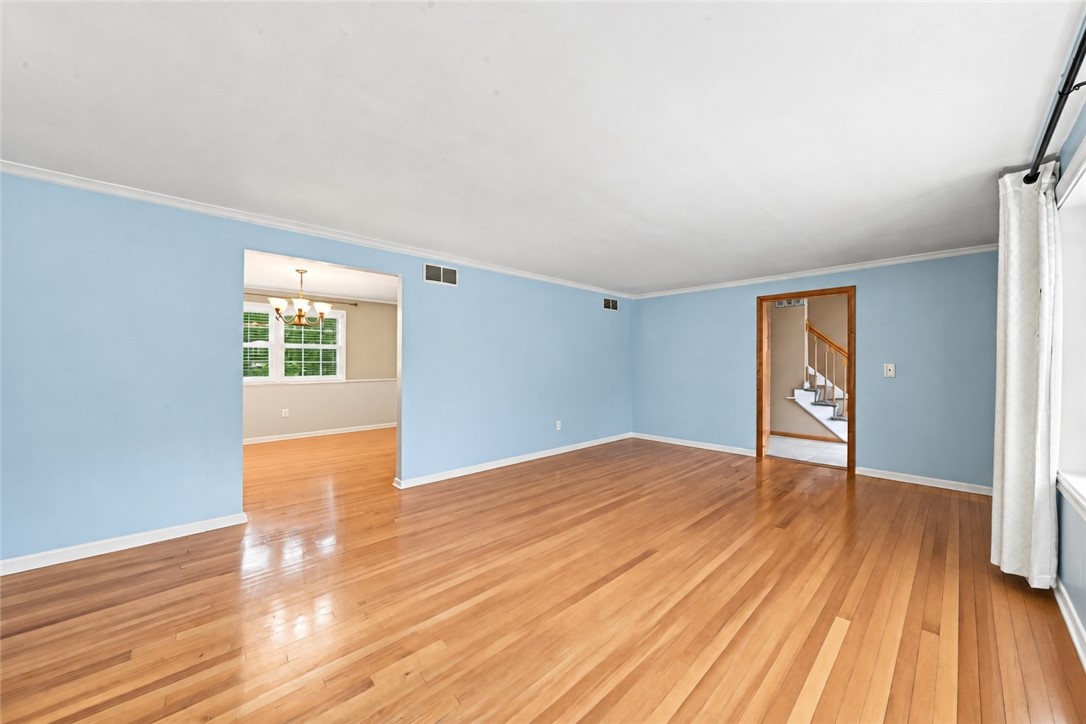 Empty living room with blue walls, polished hardwood floors, and doorways to a dining area and stairs.