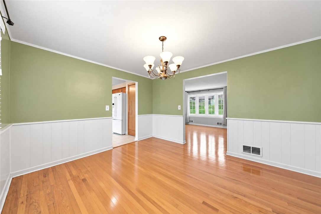 Empty dining room with hardwood floors, green walls, white wainscoting, and a chandelier.