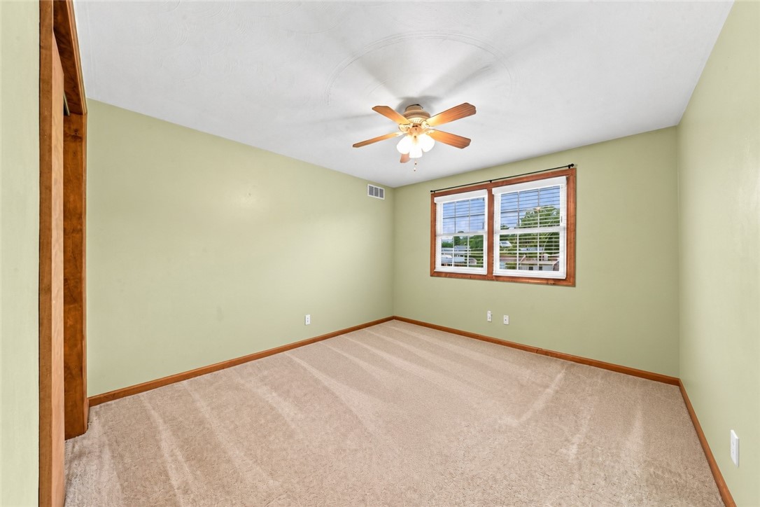 Empty bedroom with pale green walls, beige carpet, wood trim, and a ceiling fan.