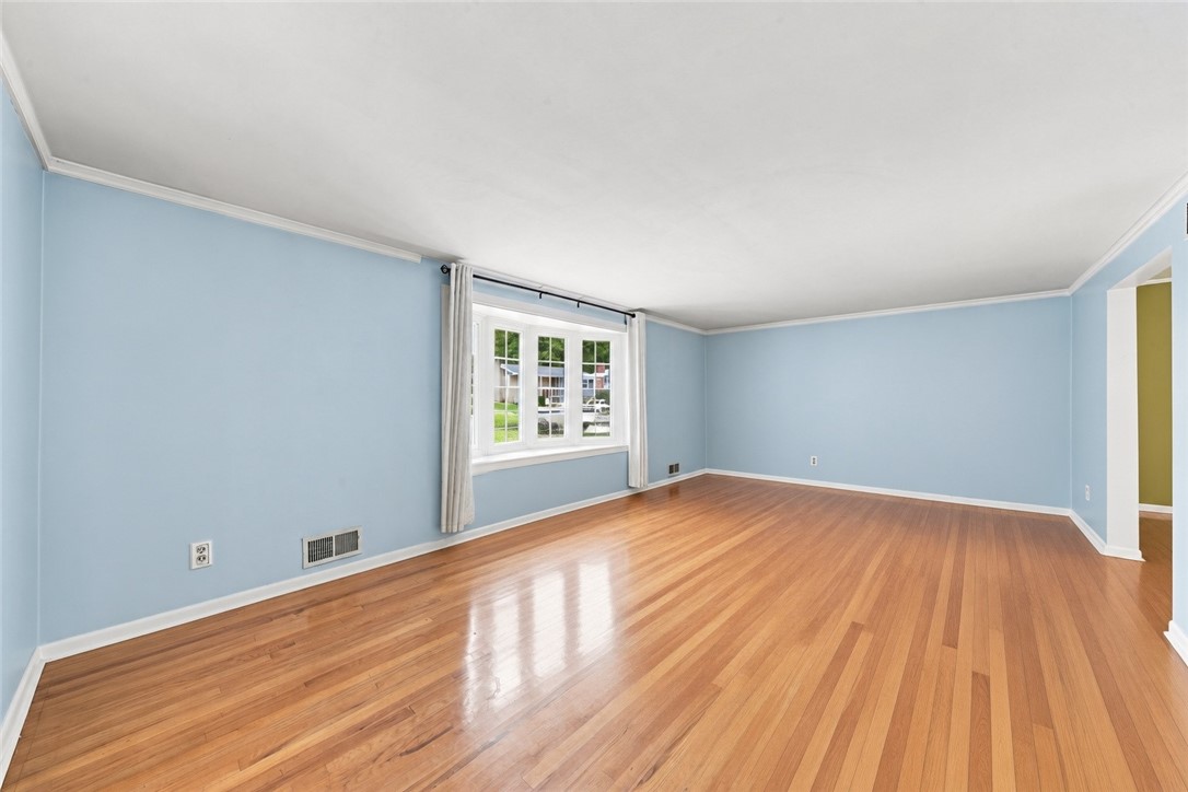 Empty living room with glossy hardwood floors, light blue walls, and a large curtained window.