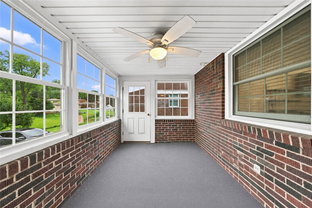 Enclosed sunroom with brick walls, large windows, gray carpet, and a ceiling fan.