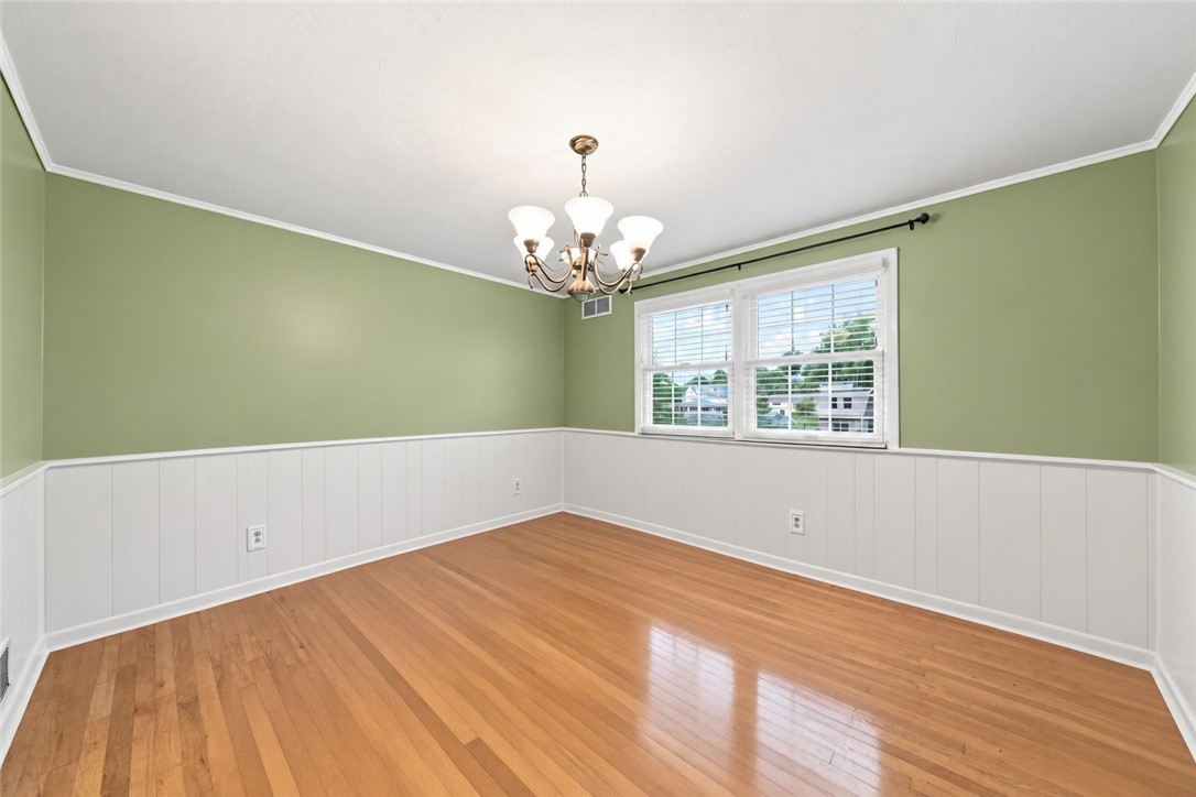 Empty dining room with sage-green walls, white wainscoting, hardwood floors, and a brass chandelier.