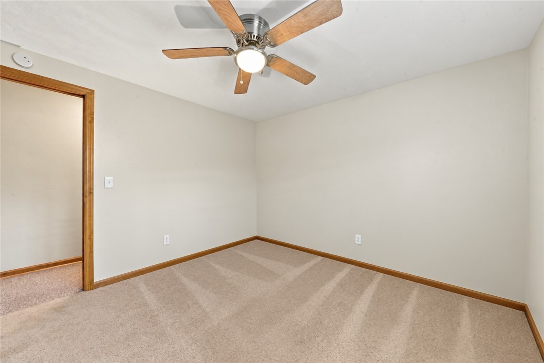 Empty bedroom with beige carpet, wood trim, and a ceiling fan with light.
