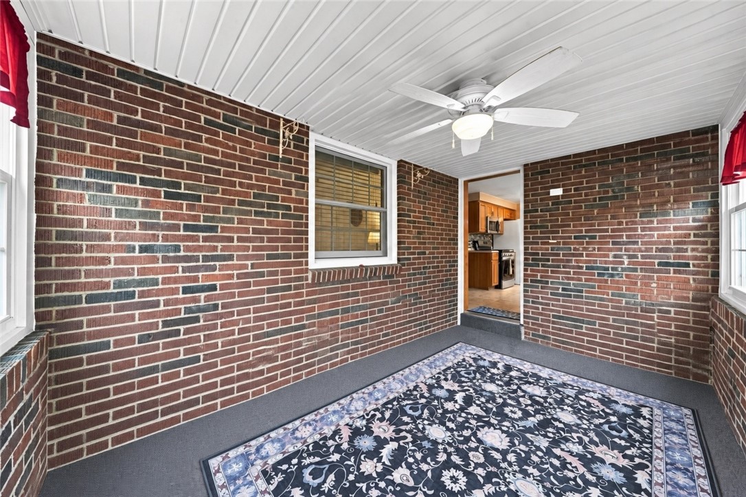 Enclosed brick porch with a white ceiling fan, patterned rug, and doorway to the kitchen.