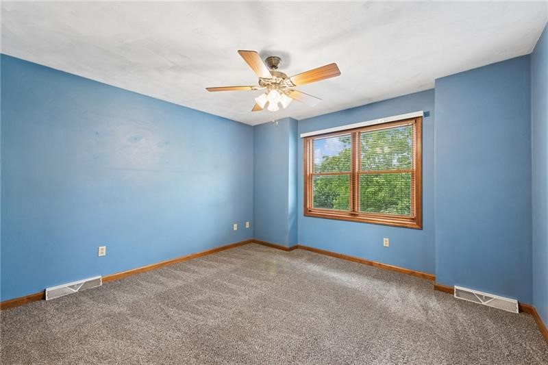 Empty bedroom with blue walls, gray carpet, and a wood-trimmed window.