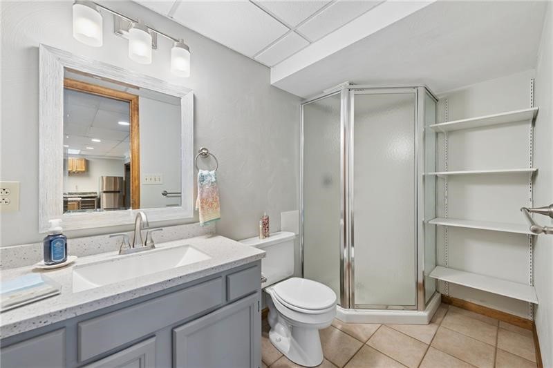 Bathroom with a gray vanity, framed mirror, glass corner shower, and open shelving.