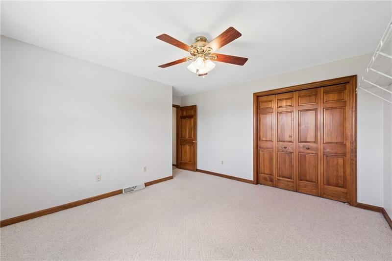 Empty bedroom with wooden closet doors, beige carpet, and a ceiling fan.