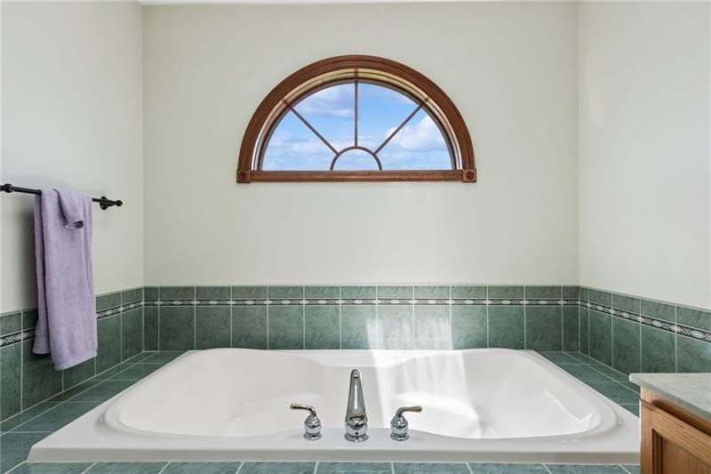 Bathroom with a large soaking tub, green tile, and an arched window.