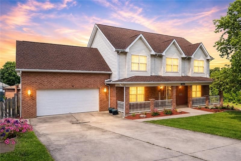 Two-story brick-and-siding home with a wide driveway, attached garage, and covered front porch at dusk.
