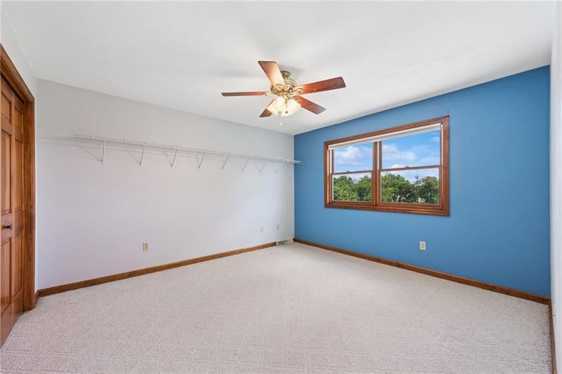Empty bedroom with a blue accent wall, wood-trimmed window, and ceiling fan.