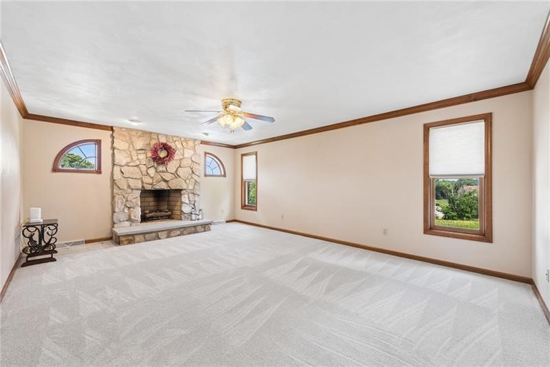 Mostly vacant living room with a tall stone fireplace, pale carpet, and dark wood trim.