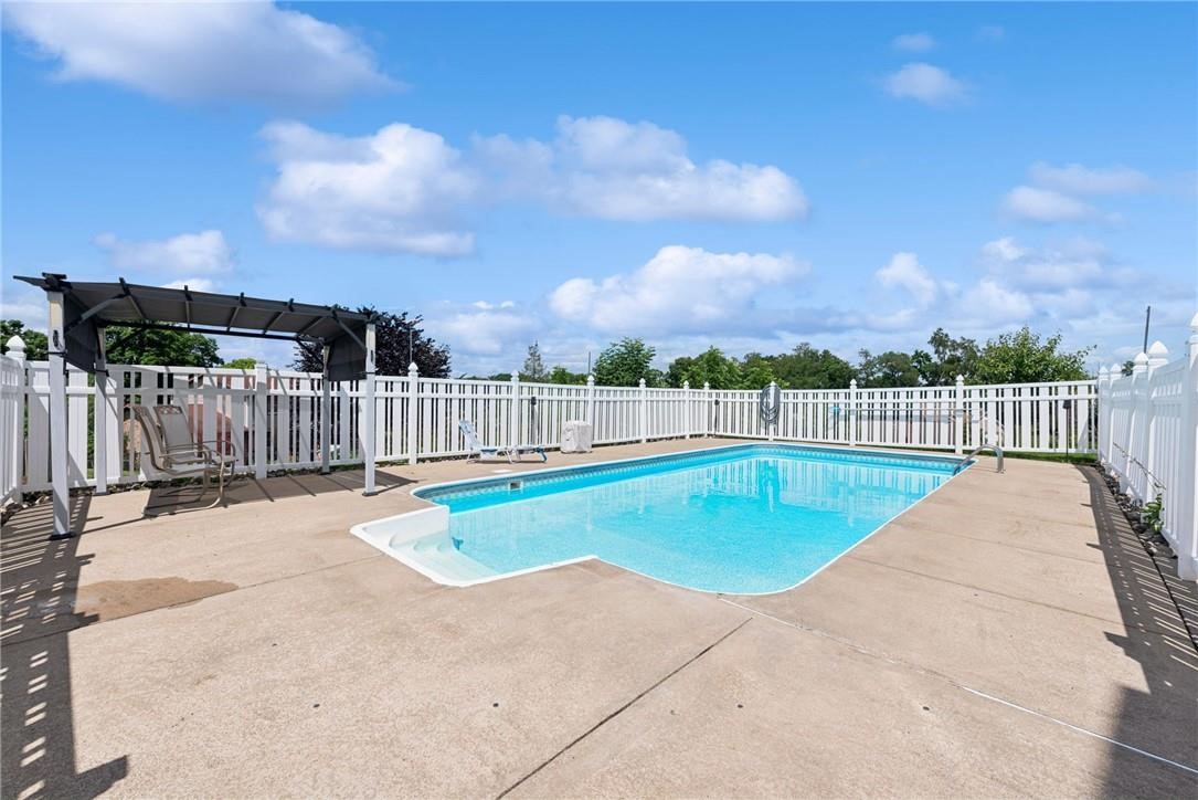 Outdoor swimming pool with a white fence, concrete deck, and shaded seating canopy.