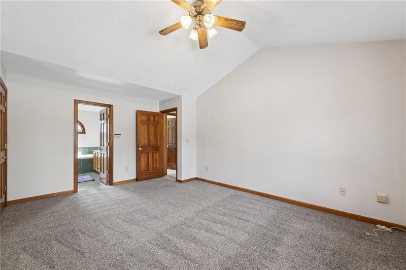 Empty carpeted bedroom with wood-trimmed doorways and a ceiling fan.