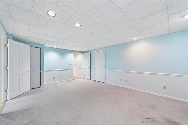 Empty carpeted room with pale blue walls, white wainscoting, recessed lights, and several doors.