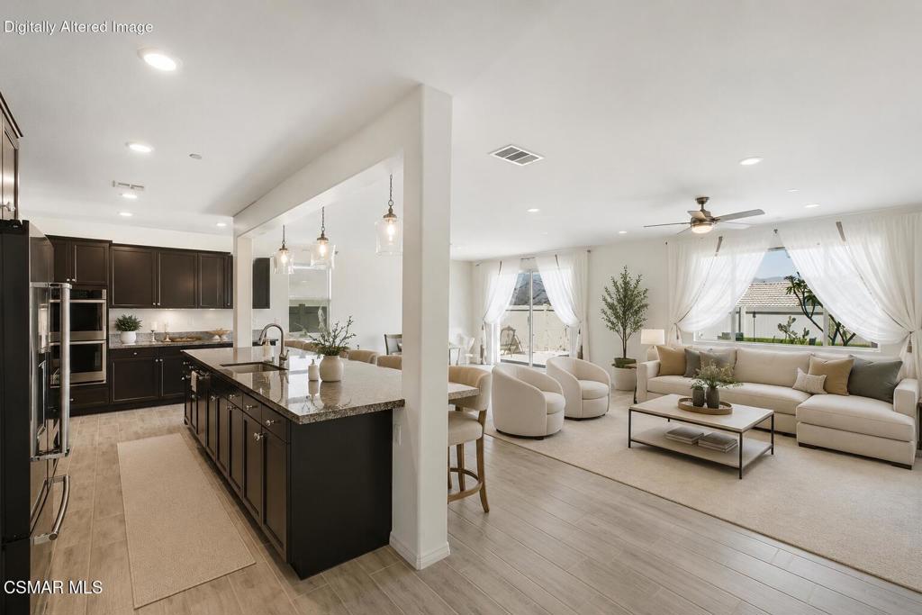 Open-plan kitchen and living room with a stone island, dark cabinets, and cream seating by wide windows.